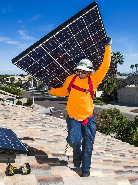 Solar service professional carrying a panel during rooftop maintenance support in Arizona